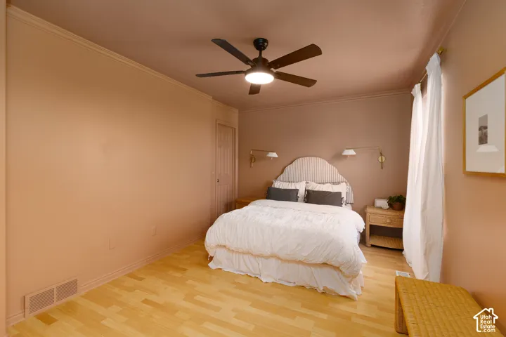 Room featuring wood-finish flooring, a matte black multi-blade ceiling fan with integrated lighting, and two gold-tone wall-mounted adjustable sconces
