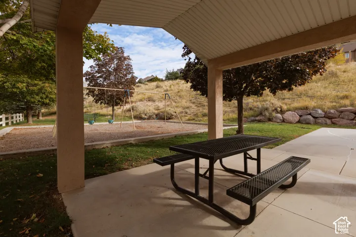 Covered concrete patio featuring a built-in metal table and bench set, landscape boulders, and mature trees