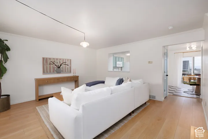 Living area featuring light wood-finish flooring, a wall-mounted pendant light fixture, and a pass-through window cutout