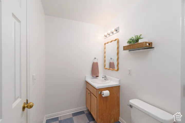 Bathroom featuring a wood-finish vanity with a white countertop, an integrated sink, a multi-bulb light fixture, and checkered tile flooring