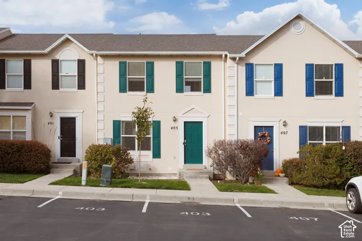 Multi-family exterior featuring light-toned stucco siding, decorative window shutters, gabled rooflines, and assigned parking spaces
