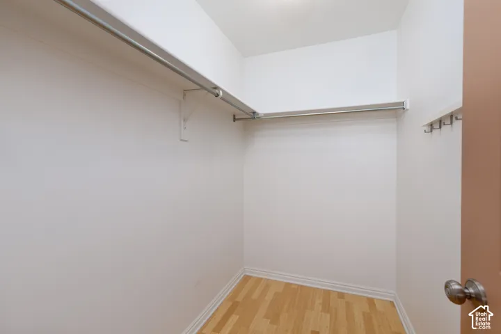 Walk-in closet featuring wood-finish flooring, white shelving, a full-width metal garment rod, and wall-mounted metal hooks