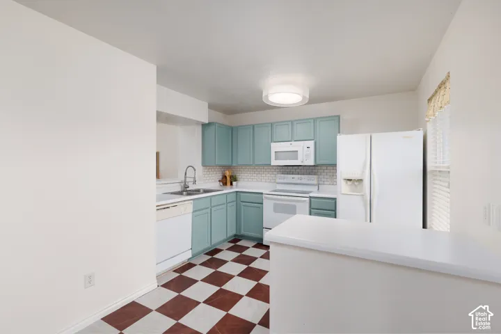 Kitchen featuring teal cabinetry, white countertops, a subway tile backsplash, white appliances, and checkerboard patterned flooring