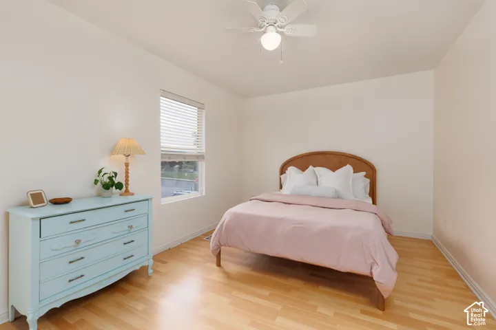Wood-finish flooring, neutral wall tones, single-pane window with horizontal blinds, and a white ceiling-mounted fan with integrated lighting