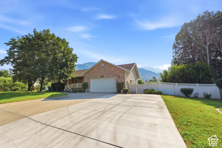 Brick exterior residence featuring an attached garage, concrete driveway, lattice-top vinyl fencing, and a mountainous backdrop