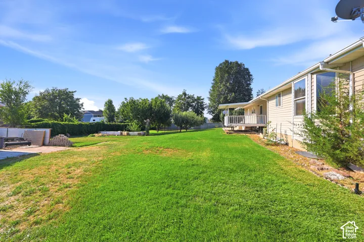 Expansive backyard featuring a large grass lawn, mature trees, a wood-railing deck, and a paved patio area