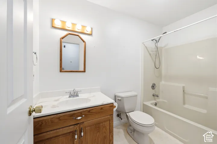 Bathroom featuring a vanity with wood-finish cabinetry, a white countertop with an integrated basin, a four-light vanity fixture, an octagonal wall-mounted mirror, and a combination bathtub and shower enclosure