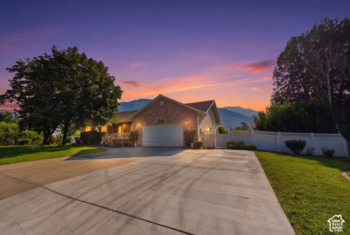 Exterior facade featuring brick masonry, a concrete driveway, a white vinyl privacy fence, and mountain scenery