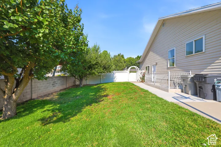 Exterior side yard featuring a concrete pathway, privacy fencing, a decorative arched gate, and mature trees
