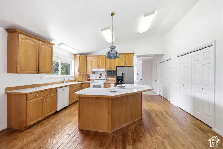 Kitchen featuring wood-finish cabinetry, a central island, wood-finish flooring, vaulted ceilings, and built-in white appliances