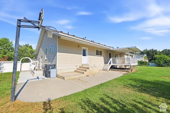 Exterior featuring vinyl siding, concrete patio, raised wood-frame deck, and white privacy fencing