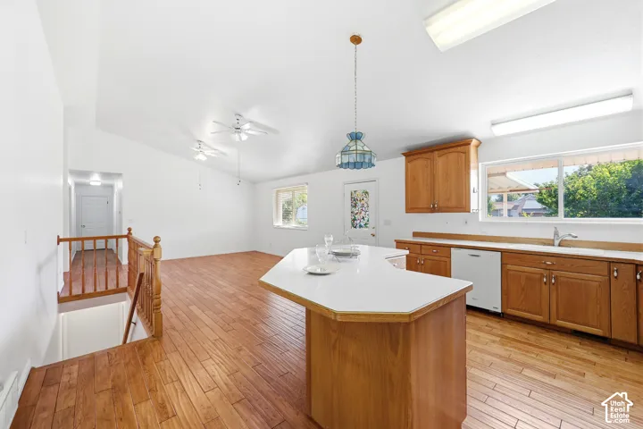 Kitchen featuring wood-finish cabinetry, an island with a light-colored countertop, wood-finish flooring, recessed ceiling lighting, and a vaulted ceiling