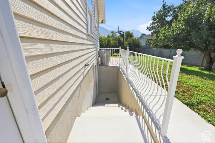 Exterior concrete stairwell with white metal railing, horizontal lap siding, and mountain backdrop