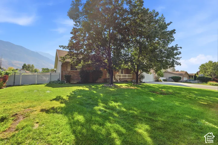Brick exterior residence featuring a front porch, an attached garage, white vinyl fencing, and mature trees against a mountain backdrop