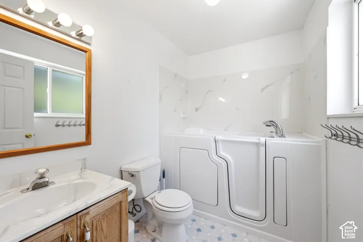 Walk-in tub with integrated faucet, wood-framed vanity, surface-mount vanity lighting, and multi-tone tile flooring
