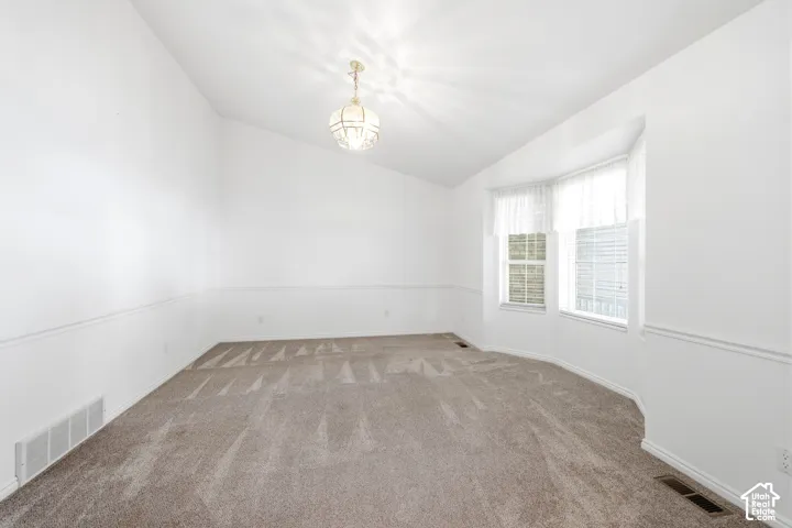 Vaulted ceilings, bay window, neutral carpeting, and decorative chair rail molding