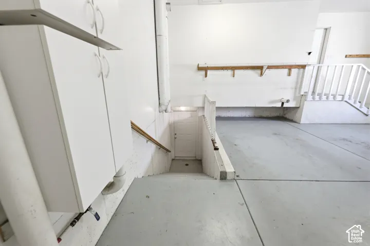 Garage interior featuring painted concrete flooring, white cabinetry, a built-in wall-mounted shelf, a staircase with a wooden handrail, and white wooden railing