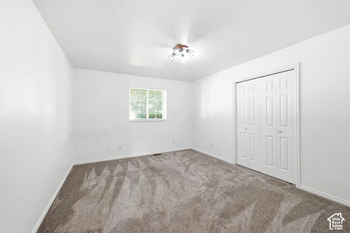 Room featuring neutral carpeting, white walls, double-door closet, multi-light ceiling fixture, and a single-pane window