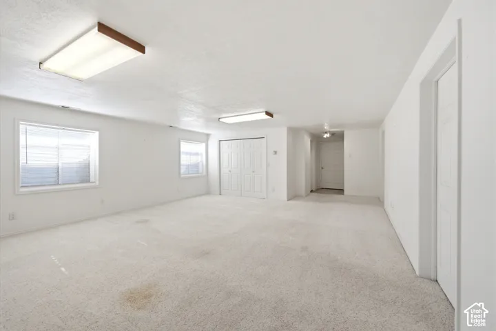 Neutral-toned interior space featuring wall-to-wall carpeting, dual recessed window wells, white paneled closet doors, and flush-mount lighting fixtures