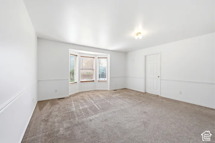 Spacious interior featuring a bay window, wall-to-wall carpeting, crisp white walls, and decorative chair rail molding