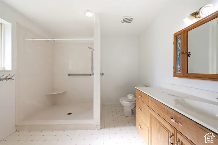 Bathroom featuring a walk-in shower with integrated corner shelving, wood-finish vanity with a molded countertop, and wall-mounted wooden cabinetry with mirror