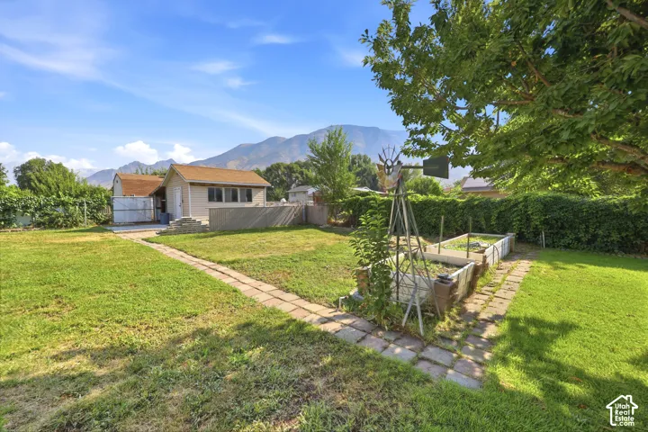 Expansive backyard featuring a stone paver walkway, raised garden beds, a decorative metal windmill, and mountain scenery