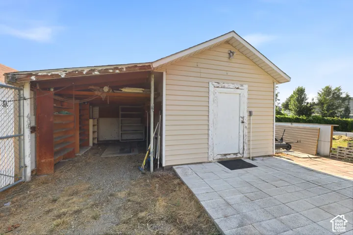 Detached outbuilding featuring horizontal lap siding, a concrete paver patio, and an open-air storage area with built-in wooden shelving