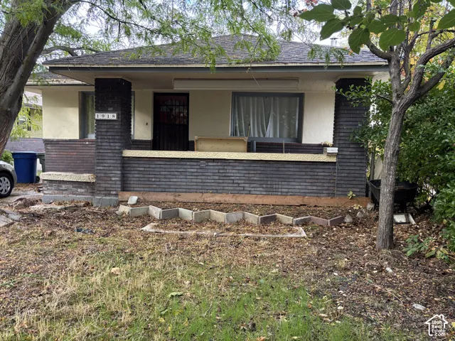 Single-story exterior featuring a covered front porch, dark-toned brick masonry, stucco siding, and a hipped roofline
