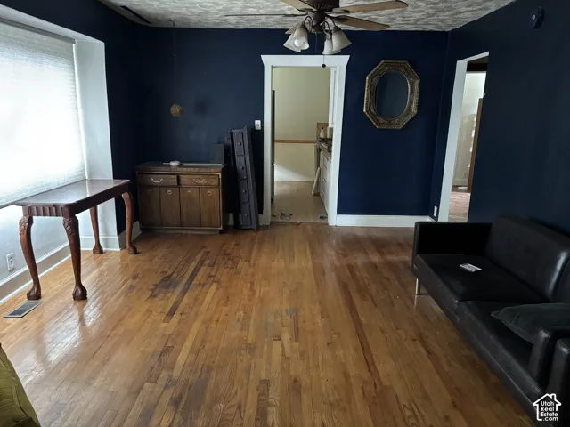 Hardwood flooring, recessed window casing, ceiling-mounted fan with integrated light fixture, and textured ceiling finish