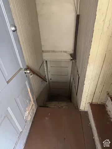 Stairway featuring vertical paneled walls, a metal handrail, and a five-panel interior door