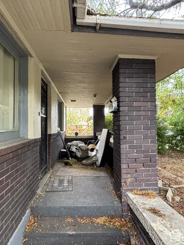 Covered front porch featuring dark brick columns, concrete steps, and a metal security screen door