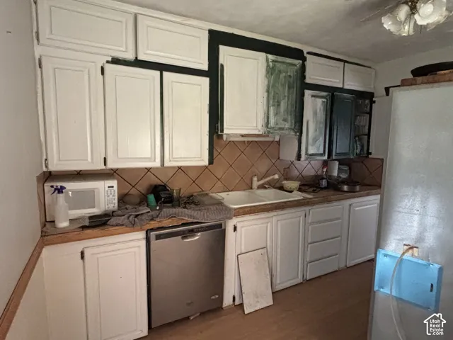 Kitchen featuring white cabinetry, wood-finish countertops, a dual-basin sink, a stainless steel dishwasher, and a diamond-pattern tile backsplash