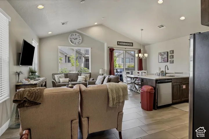 Open-concept interior featuring vaulted ceilings, recessed lighting, tile flooring, and a kitchen island with stone-surface countertops and an integrated stainless steel sink