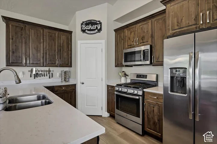 Kitchen featuring stained wood cabinetry, stainless steel appliances, quartz countertops, dual-basin stainless steel sink, and wood-finish flooring