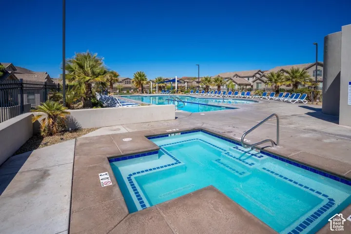 Outdoor spa with tile border and concrete deck, featuring a swimming pool, metal security fencing, and mature palm trees