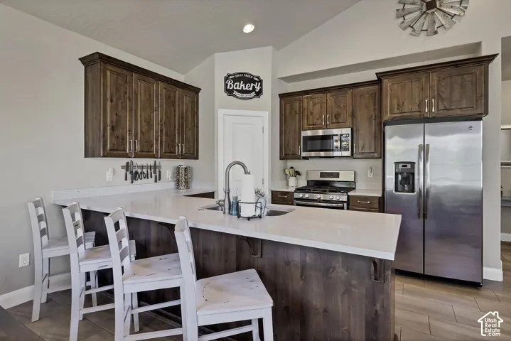 Kitchen featuring stained wood cabinetry, stone countertops, stainless steel appliances, a vaulted ceiling, and wood-finish tile flooring