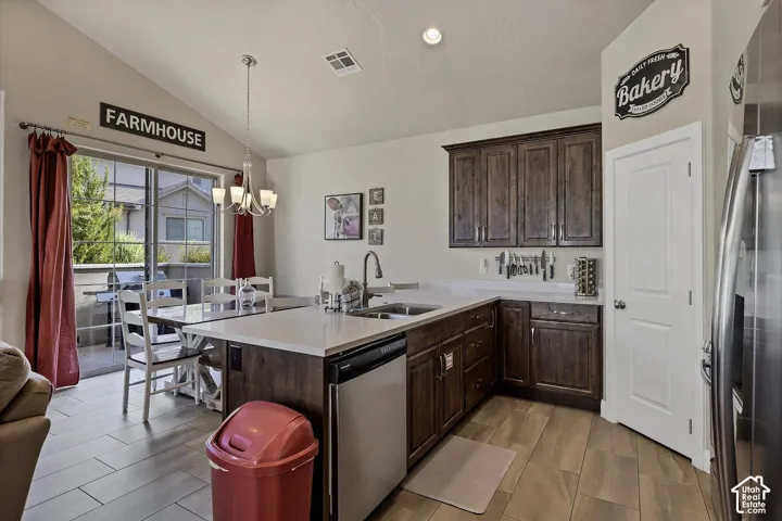 Kitchen featuring dark wood-finish cabinetry, light-toned stone-finish countertops, stainless steel appliances, a multi-light pendant fixture, and wood-finish tile flooring