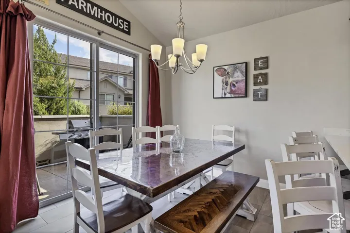 Vaulted ceiling, multi-light chandelier, sliding glass door, and tile flooring