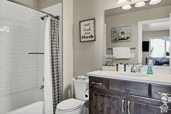 Full-width vanity featuring a stone countertop, an integrated oval basin, stained wood cabinetry, and a wide-format vanity mirror with integrated light fixture, featuring a bathtub with white subway tile surround