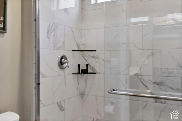 Walk-in shower featuring large-format stone-patterned wall tile, frameless glass door, chrome fixture, and built-in glass corner shelving