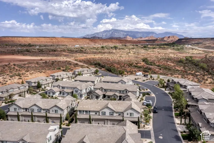 Aerial perspective of residential multi-unit structures featuring multi-gable rooflines, light-toned siding, and paved driveways, set against a backdrop of desert terrain and mountain topography
