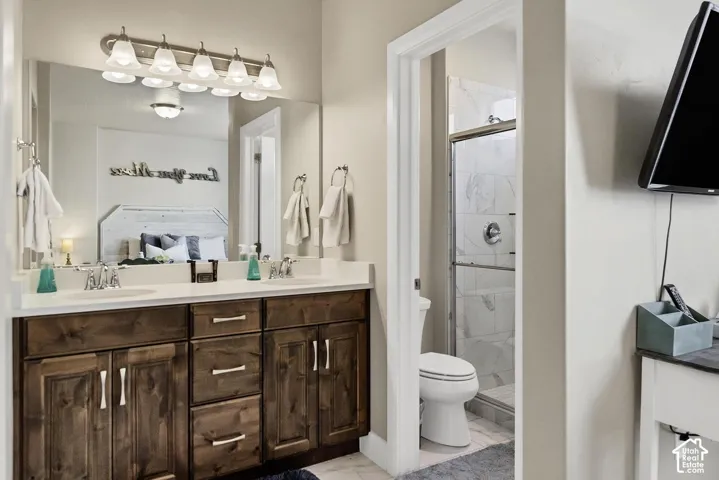 Double vanity with stained wood cabinetry, solid surface countertop, wall-to-wall mirror, six-light fixture, and shower enclosure with tile surround