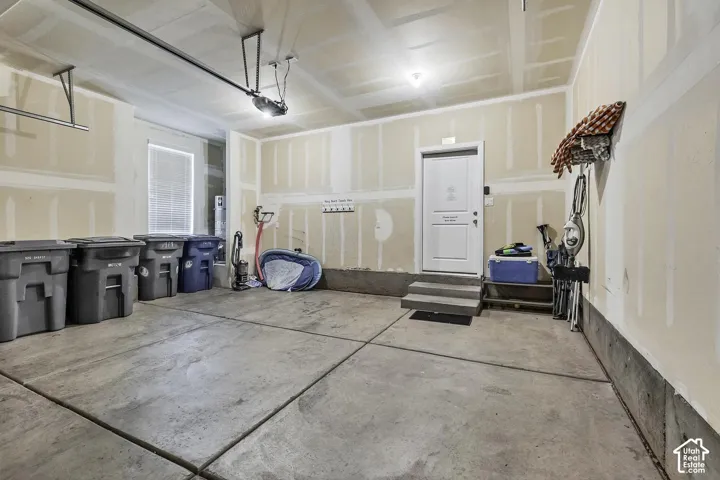 Multi-car garage featuring a concrete floor, drywall finish, and direct-access exterior door with concrete steps