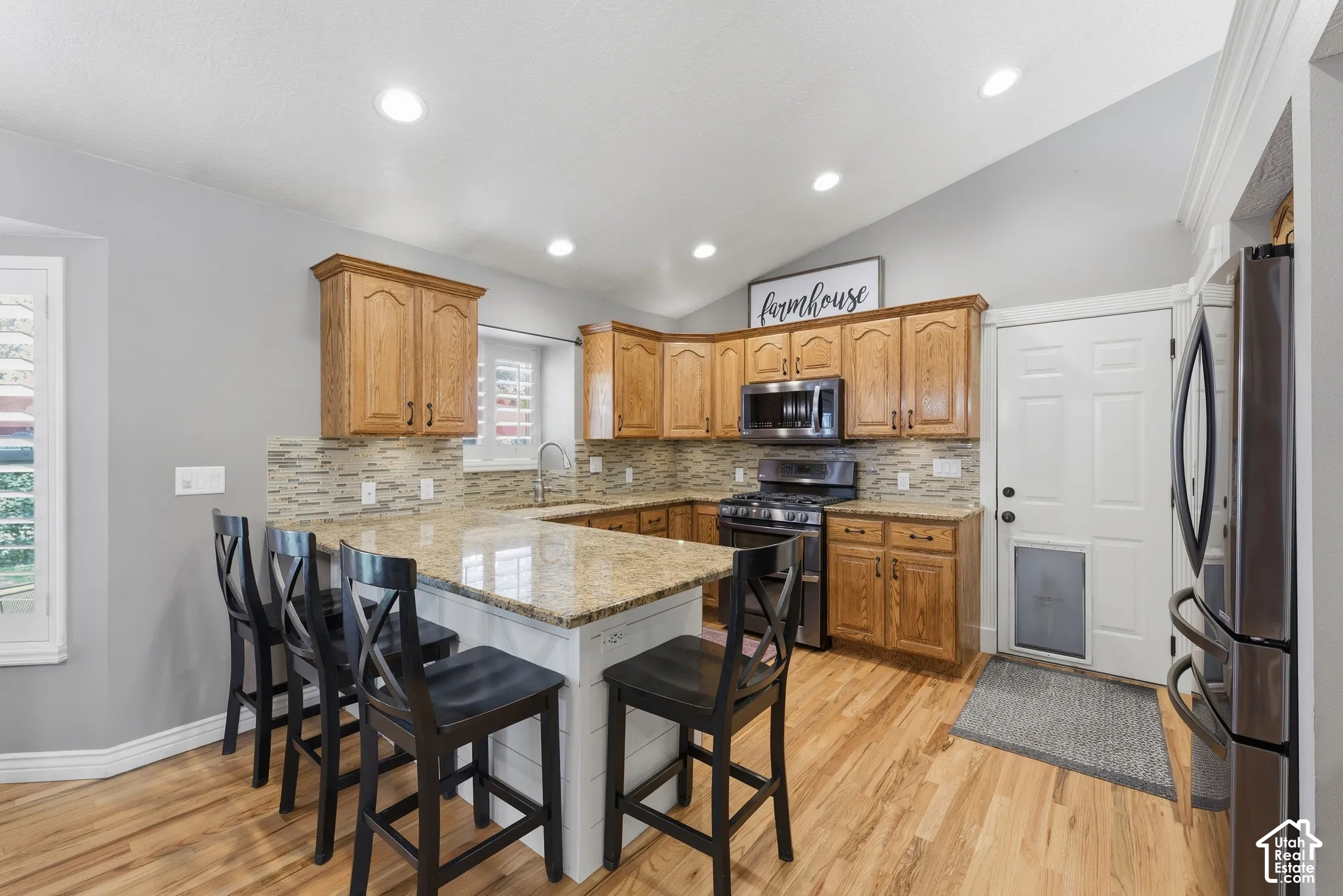 Kitchen featuring vaulted ceilings, wood cabinetry, stone countertops, a multi-tonal linear tile backsplash, and wood-finish flooring