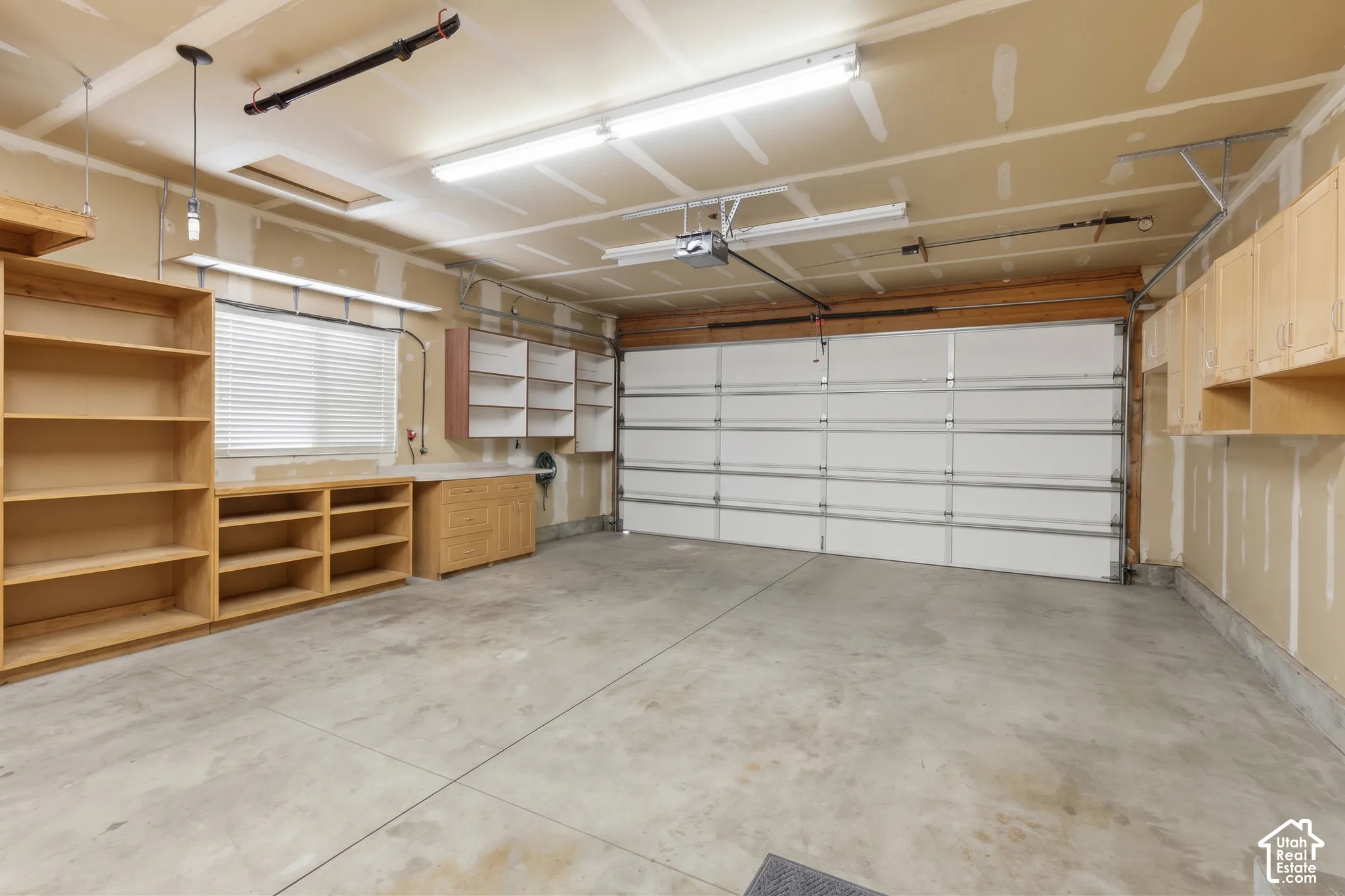 Multi-car garage featuring concrete flooring, extensive built-in wood-finish shelving and cabinetry, a wide overhead paneled door, and overhead fluorescent lighting