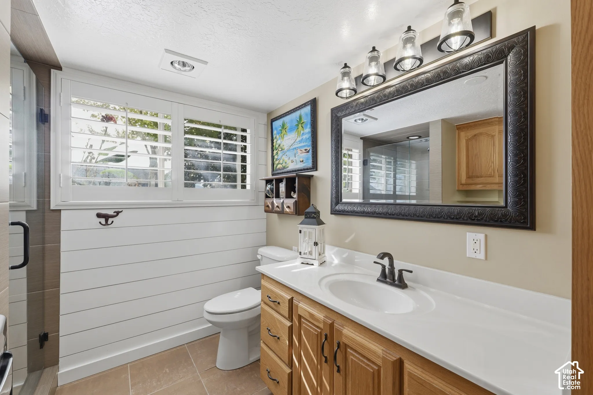 Bathroom featuring white shiplap wall paneling, plantation shutters, custom wood cabinetry, an integrated sink, and four-bulb overhead vanity lighting