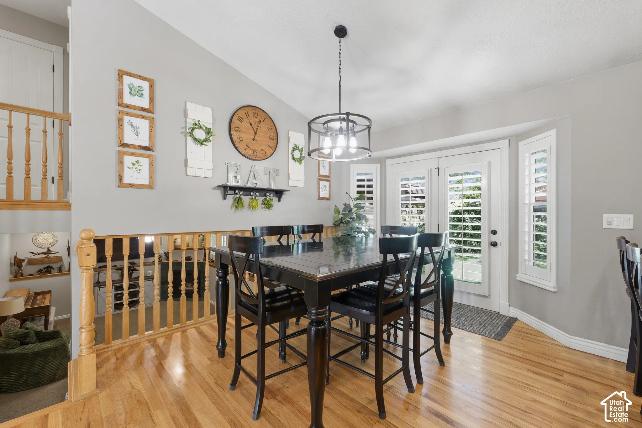 Dining area featuring wood-finish flooring, vaulted ceilings, a metal drum chandelier, and double doors with plantation shutters