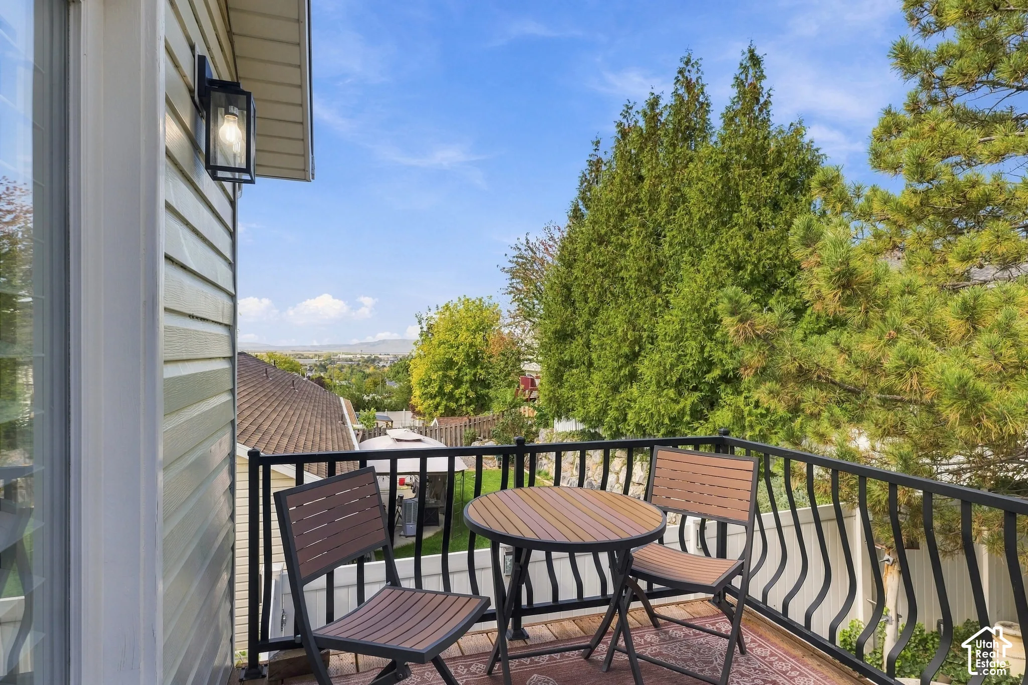 Elevated wood-deck balcony featuring a black metal railing and exterior wall-mounted lantern light