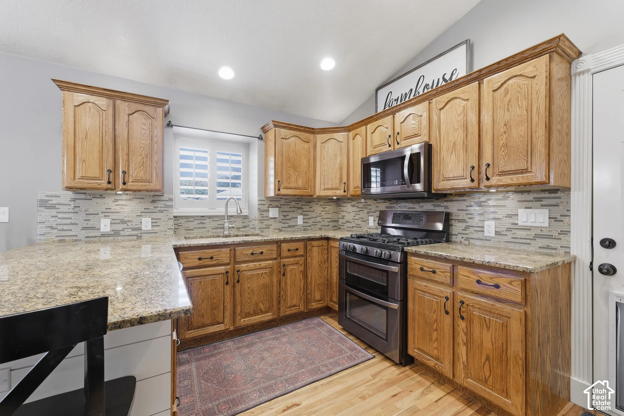 Kitchen featuring wood cabinetry, stone countertops, integrated stainless steel appliances, multi-toned mosaic tile backsplash, and wood-finish flooring