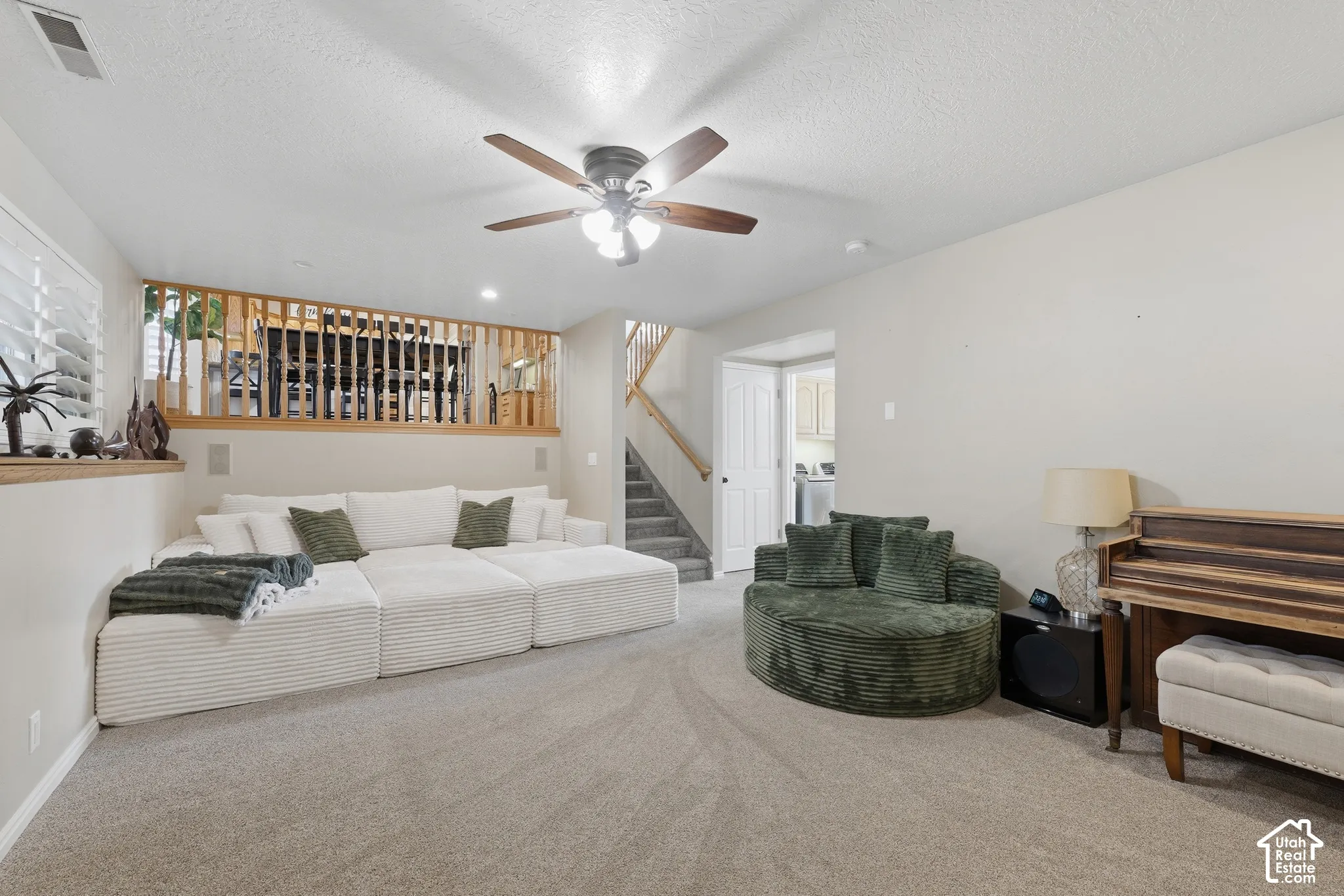 Carpeted flooring, ceiling-mounted fan with integrated lighting, wood-railing staircase, and wood-finish balustrade feature